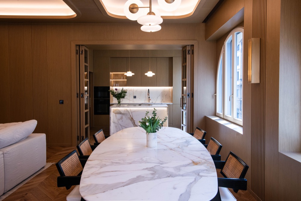 Dining room with a table for eight, a tall arched window, and the kitchen beyond